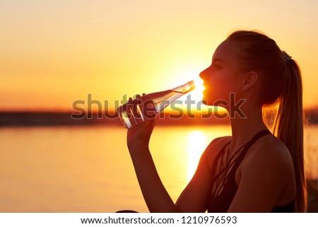 Silhouette woman drinking water from bottle after run or yogaon the beach. Fitness female profile at sunset, concept of sport and relaxation