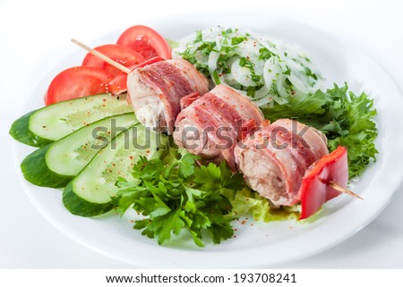 skewers wrapped in bacon with tomatoes, cucumbers, greens
