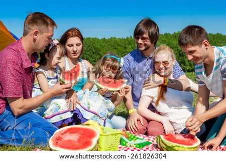 outdoor group portrait of happy family having picnic on green grass in park and enjoying watermelon