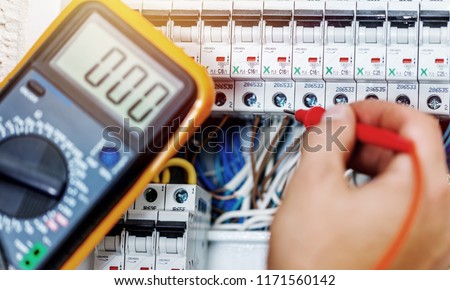 Hand of an electrician with multimeter probe at an electrical
