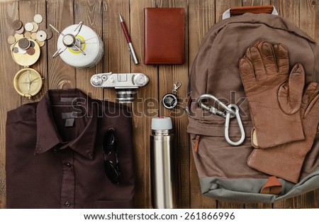 Antique. Overhead view of hiking gear laid out for a backpacking trip on a rustic wood floor. Items include, Backpack, gloves, sweater, camera, film, binoculars, passport, wallet, canteen, compass