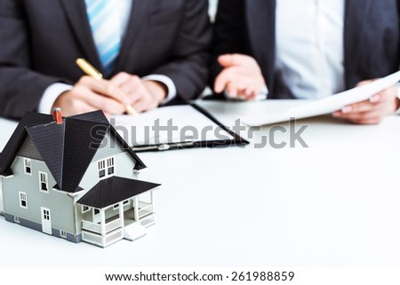 Agency. Businessman signs contract behind home architectural model