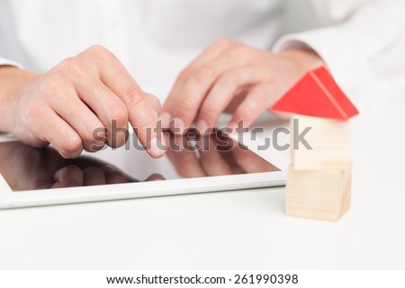 Home. Conceptual image of a man signing a mortgage or insurance contract or the deed of sale when buying a new house or selling his existing one with a small wooden model of a house alongside