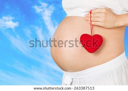 Expecting. Close up on pregnant belly. Woman expecting a baby holding a red heart with love.