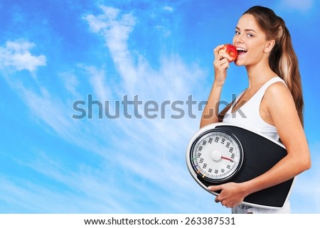 Exercising. Beautiful young woman holding measuring instrument and eating an apple