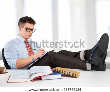 Men. Writer at work. Handsome young man in shirt and suspenders writing something in notebook while sitting at his working place