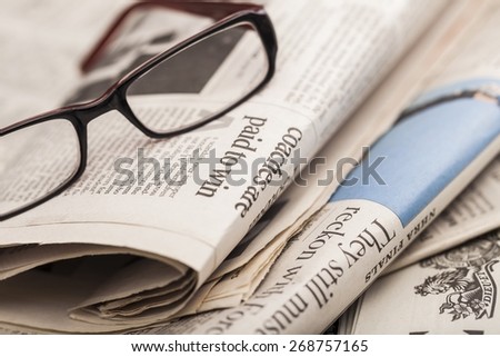 News. Reading glasses lie on newspaper pile