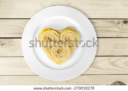 Pasta. Cooked spaghetti carefully arranged in  heart shape and topped with tomato sauce, on color background