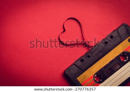 Music. Valentines day card. Vintage audio cassette with loose tape shaping a heart on red background