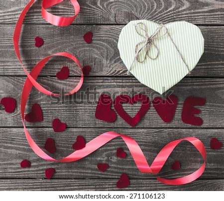Love. Word Love with Heart shaped Valentines Day gift box on old vintage wooden plates. Sweet holiday background with rose petals, small hearts, curved ribbon.