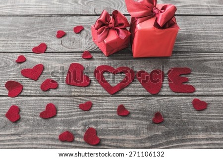Love. Word Love with Heart shaped Valentines Day gift box on old vintage wooden plates. Sweet holiday background with rose petals, small hearts, curved ribbon.