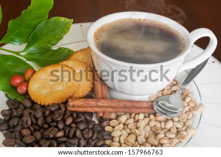 Smoking hot coffee, Black beans, White beans, Ripe coffee beans , coffee leafs,Cinnamon and Cracker on Plate.