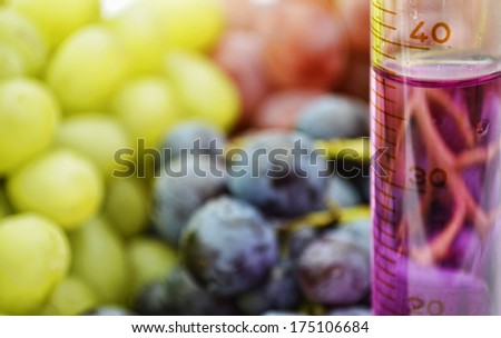 Grape extract in a graduated cylinder with red green and blue grapes in the background