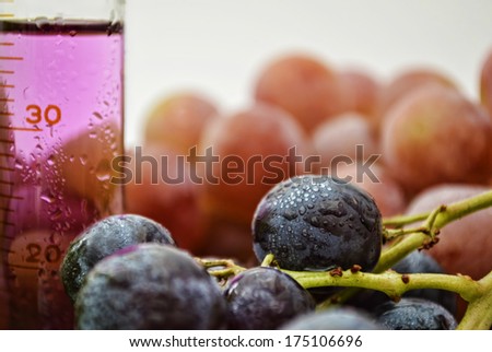 Grape extract in a graduated cylinder with red and blue grapes in the background