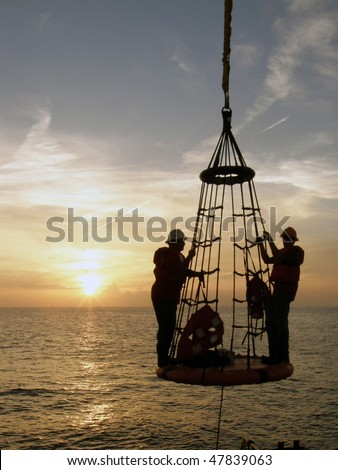 Offshore oil field workers being lowered from the rig to a boat below