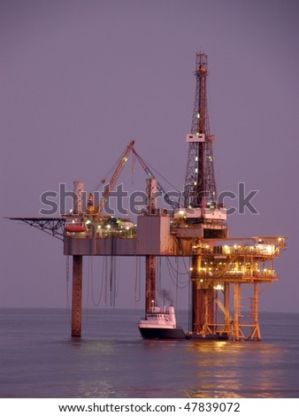 Offshore oil platform, drilling rig, and supply boat at twilight