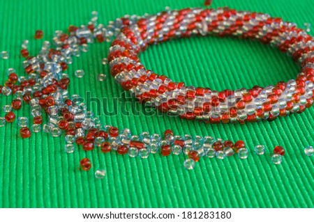 Knitted bracelet from red and gray beads on a green background