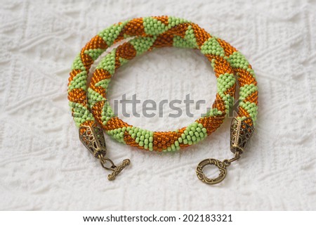 Knitted necklace from beads of light green and orange color
