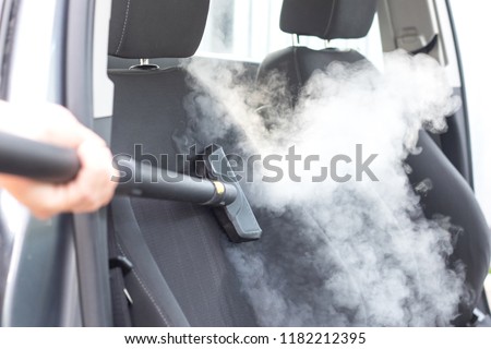 Man\'s hands holding a steam cleaner cleaning stinky car interior, lots of vapor, clean without chemicals concept
