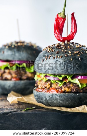 Close up delicious hot spicy black burger with chili pepper on craft paper on cutting board on white wood table