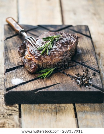 Grilled beef steak with salt, pepper and rosemary on meat cutting board on dark wooden background
