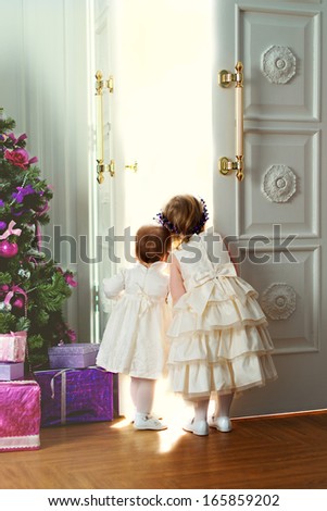 Two little sisters opening the doors and looking out something magic near the Christmas tree