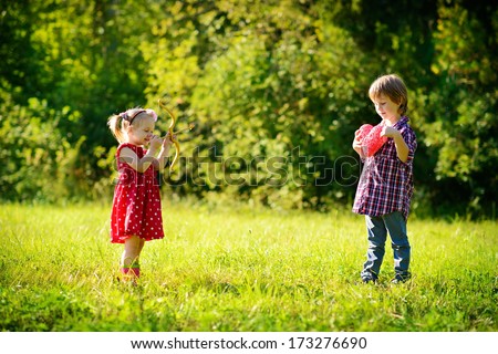 A little cute girl and a boy playing with a bow and arrows in the green meadow on a sunny summer day as if they were in love with each other