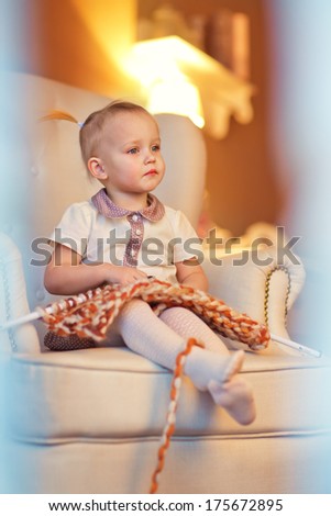 A 3 year old little girl sitting on the couch and learning to knit.