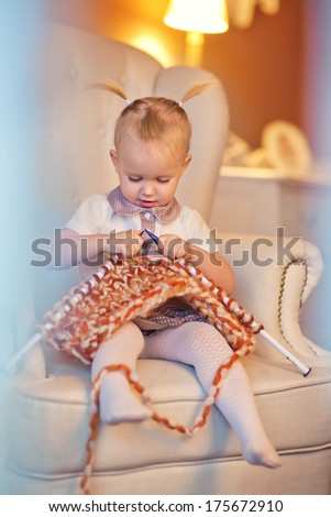 A 3 year old little girl sitting on the couch and learning to knit.