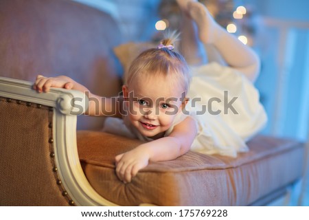 A lovely 3 year old girl in a beautiful white dress lying on a sofa and imagining herself as a gymnast