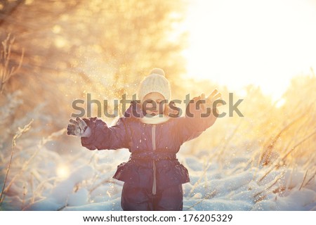 A cute smiling child in the warm clothing playing with snow on a frosty winter day