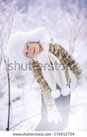 A cute boy in a white fur cap with ear-flaps on a frosty winter day