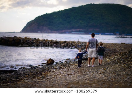 Back view of a father and his kids walking on the sea shore
