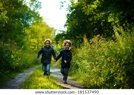 Two brothers running in the green wet forest after the rain on a sunny summer day
