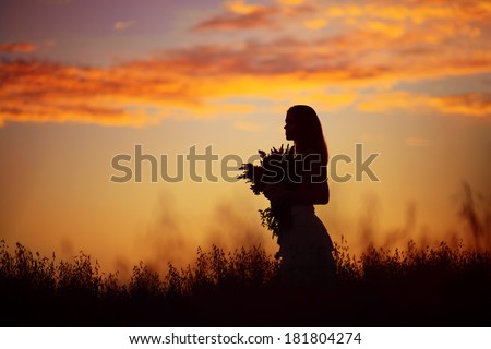 A silhouette of a beautiful girl holding flowers in the meadow at magnificent sunset