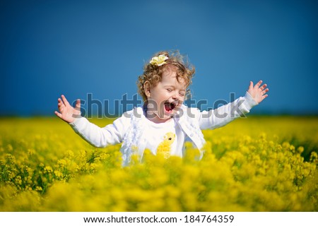A beautiful little curly laughing girl jumping happily among bittercress flowers in the meadow in a sunny summer day