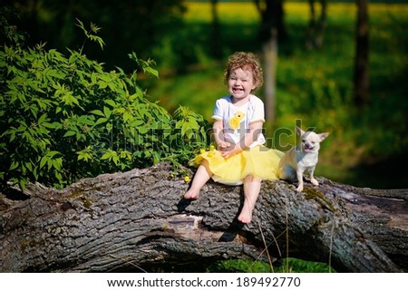 A happy little curly laughing girl with a little dog sitting on the snag in the forest in a sunny summer day