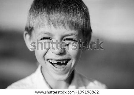 A laughing child without teeth with a ladybird on his cheek close up,  black-and-white photo