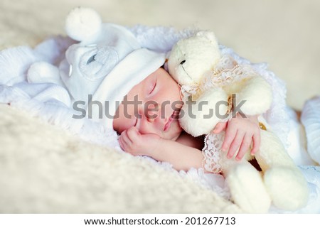 A portrait of a cute newborn baby in a blue like a bear cub hat sleeping with a white teddy bear