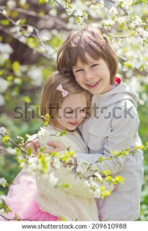 A lovely little girl and a cute boy embracing under a blooming cherry tree in a sunny spring day. Kids and flowers closeup