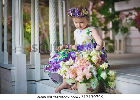 A little sweet girl with a flower diadem near the white beautiful house decorated with flowers in a sunny summer day.