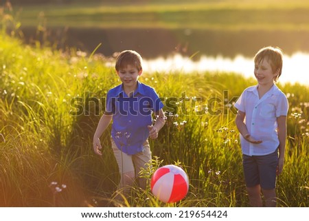 Two young cute boys playing ball on the riverbank on a sunny summer day. Kids in country. Friendship. Brothers. Nature.