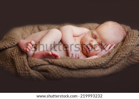A cute new-born baby sleeping on a knitted brown cushion on black background.