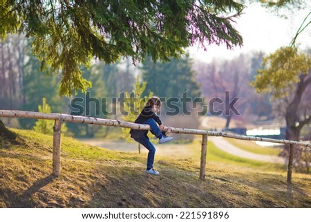A young cute boy climbing over the fence in country. Kids and nature.