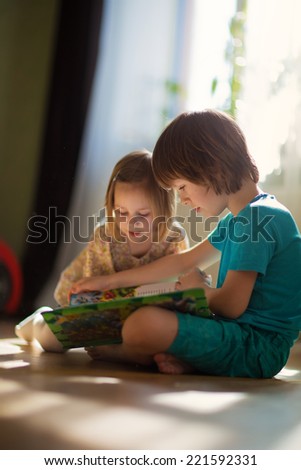 Two little cute kids reading a book sitting on the floor. Happy family.