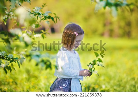 A lovely little girl standing under a blooming apple tree on a sunny spring day. Kids and flowers closeup