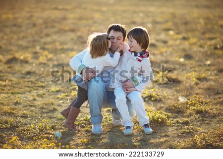 Happy family: young father with his little children walking in the field in summer morning. Strong healthy daddy hugging his daughter and his son.