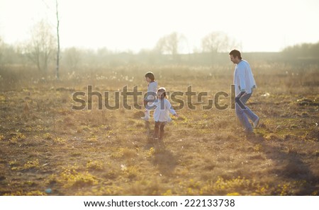 Happy family: young father with his little children walking in the field in summer morning. Strong healthy daddy playing with his daughter and his son.