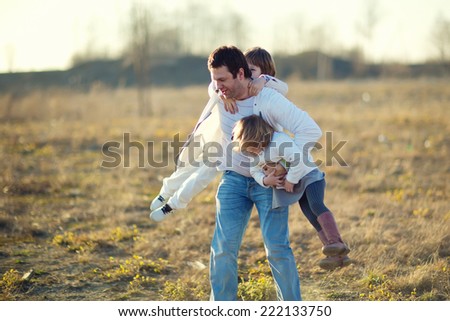 Happy family: young father with his little children walking in the field in summer morning. Strong healthy daddy spinning with his daughter and his son.