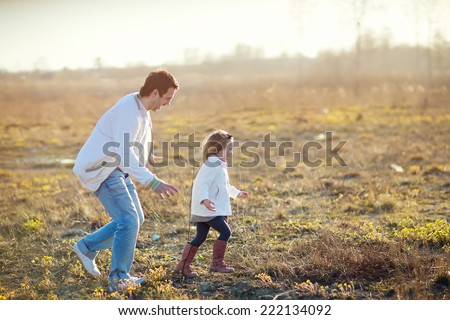 Happy family: young father with his little children walking in the field in summer morning. Strong healthy daddy playing with his daughter.